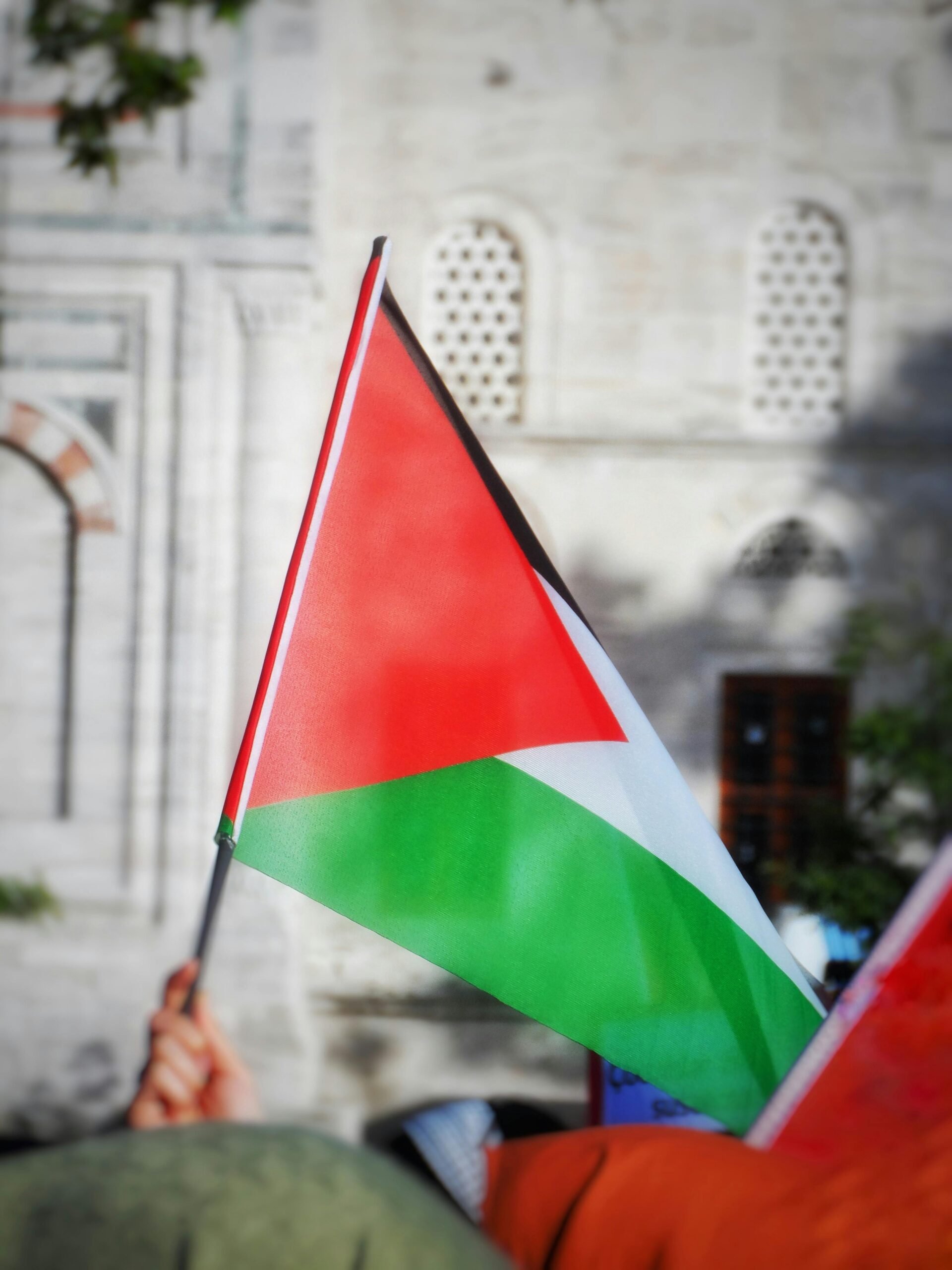 Palestinian flag waving outside historic building, symbolizing cultural pride.