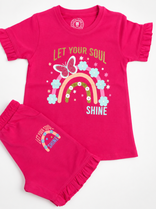 Cute little girl wearing pink rainbow print t-shirt with matching frill shorts in a cozy grey and white studio background, stylish cotton summer outfit for kids